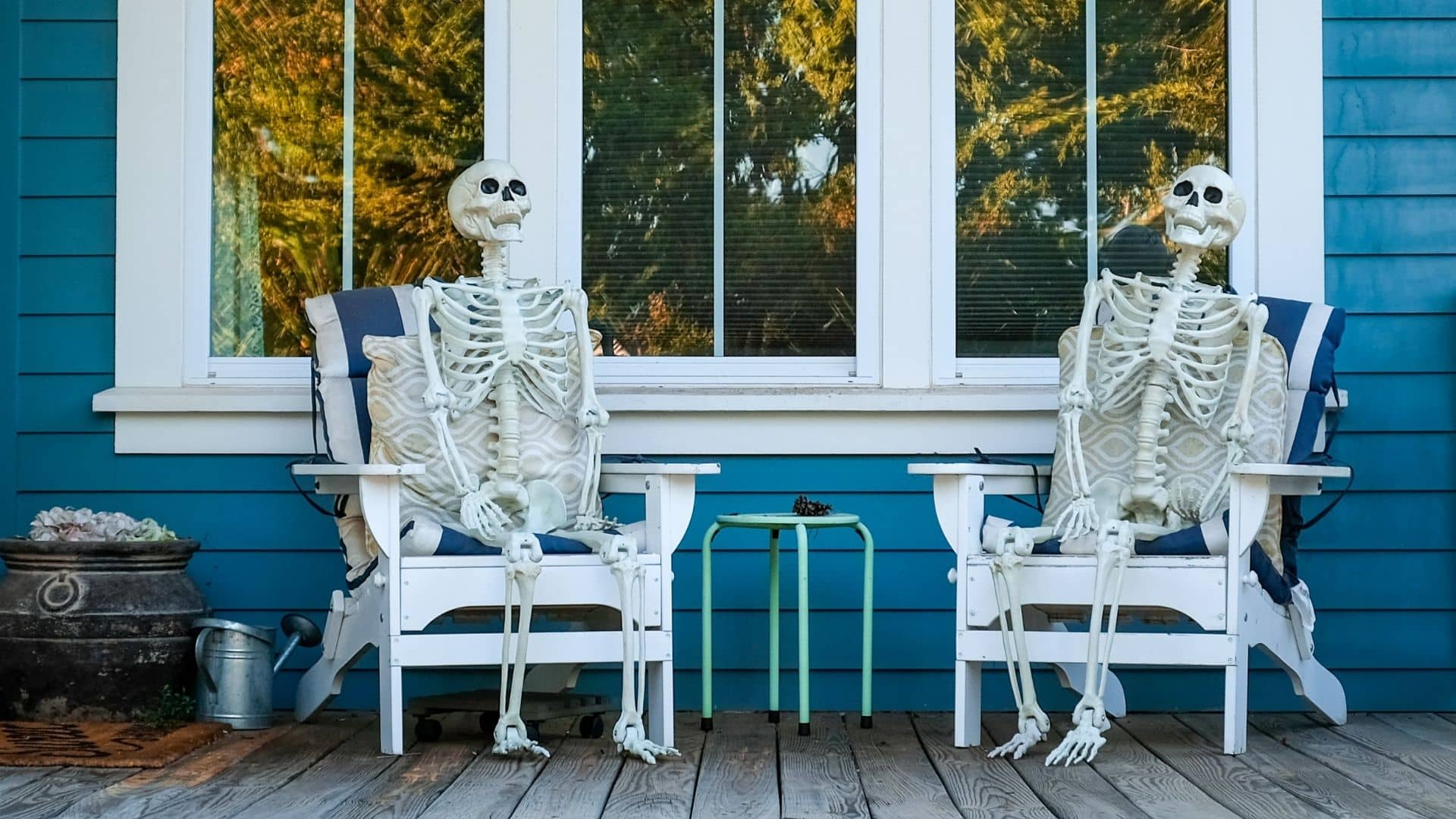 two skeletons sit in chairs on a front porch